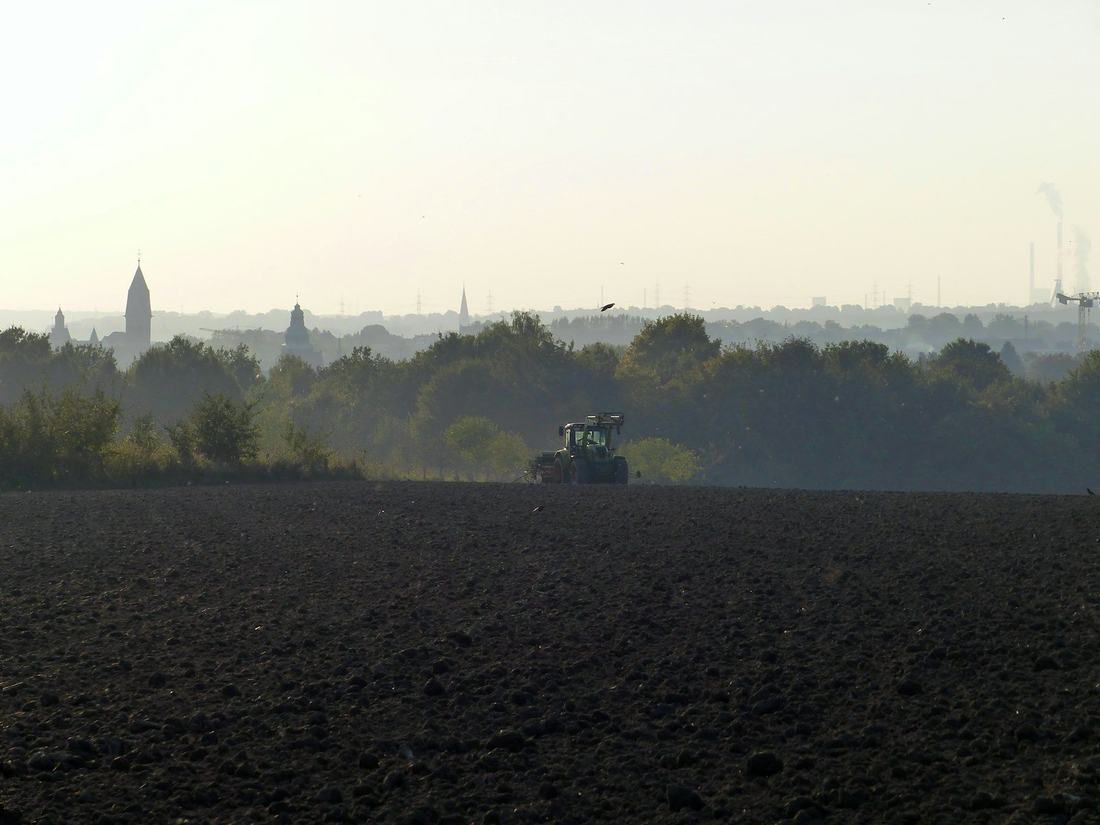 Ciągnik na ciemnym polu w oddali, za nim wieś z kościołem