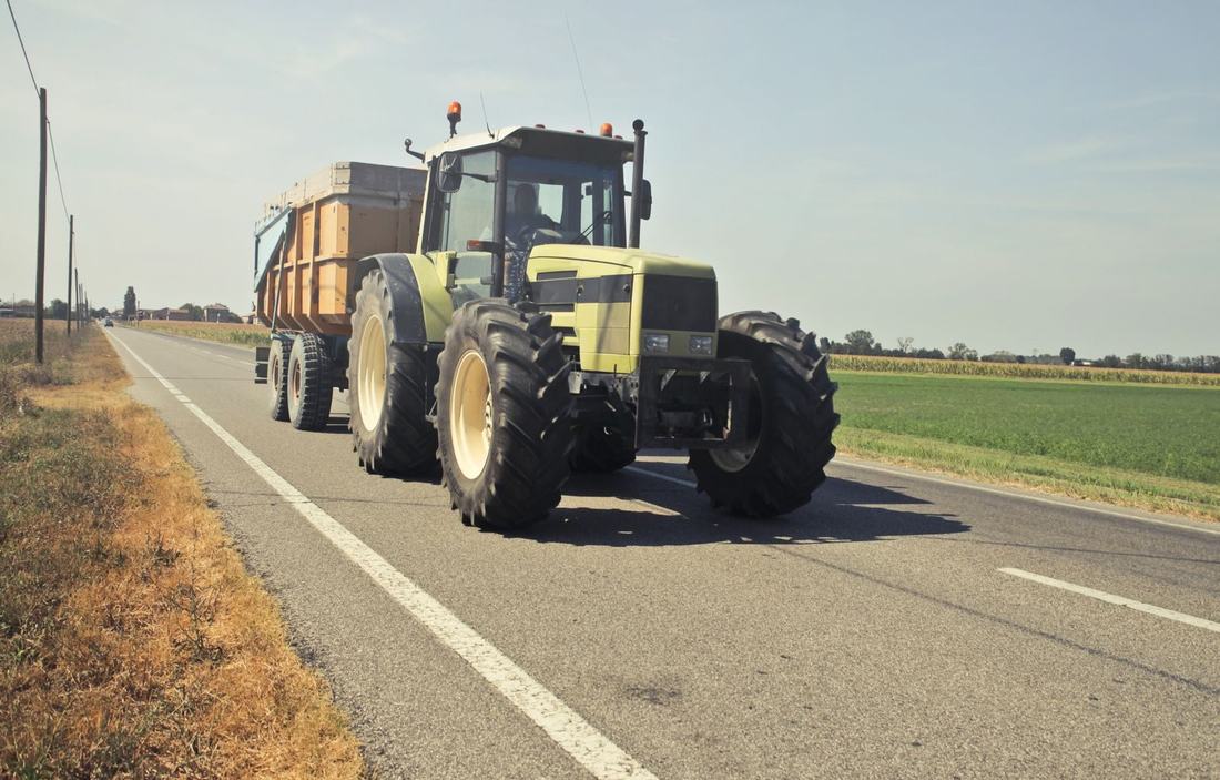 Ciągnik z przyczepą jedzie drogą między polami