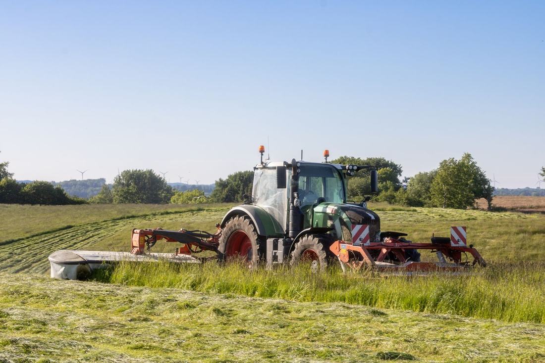 Ciągnik z kosiarką kosi łąkę na skraju doliny